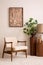 Stylish composition of elegant living room with beige armchair, brown mock up poster frame, carpet, plant and carpet. Cozy home