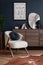 Stylish composition of elegant living room interior design with fluffy armchair, wooden commode, mock up poster frame. Temnplate.