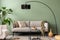 The stylish composition at living room interior with green wall, design gray sofa, coffee table, dark lamp and elegant personal