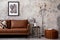 The stylish composition of living room interior with mock up poster frame, modern brown sofa, pouf, minimalistic lamp, round