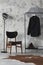 The stylish compostion at living room interior with concrete wall, chair, hanger with clothes and elegant personal accessories.