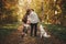 Stylish couple kissing and standing with cute dog in sunny autumn woods. Young  hipster family hiking with swiss shepherd white
