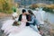 Stylish couple newlyweds are relaxing on a plaid and sitting before a lake. Bride and groom with dreadlocks are posing