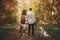 Stylish couple standing with cute dog in sunny autumn woods. Young  hipster family hiking with swiss shepherd white dog. Traveling