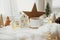 Stylish cup of tea with modern christmas houses, pine cone, wooden star and tree decor, golden lights on warm blanket on