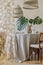 Stylish dining room interior with wooden table, design chairs, rattan pendant lamps, tropical leafs in vase and elegant decoration