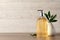 Stylish dispenser with liquid soap and green leaves in vase on wooden table, space for text