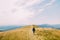 Stylish dressed man, holding a bottle of wine closing to hill with lone girl in white dress under amazing cloudy sky