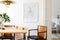 Stylish and eclectic dining room interior with mock up poster map, sharing table design chairs, gold pedant lamp and elegant sofa