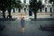 A stylish elegant girl in a dark dress with blond hair stands beautifully in a park alley on a city street