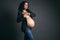 Stylish ethnic pregnant woman in gray blazer and casual jeans, shows her smart watch smiles at camera, studio background