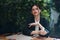 Stylish fashion woman sits in a cafe at a table and smokes a cigarette releasing smoke from her mouth with red lipstick