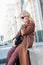 Stylish fashionable blonde woman wearing coat and sunglasses speaking on mobile phone, street style photo