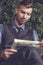 Stylish fashionable brutal handsome businessman sits in chair and reads news in newspaper. Portrait of man in suit