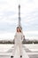 Stylish female person standing near Eiffel Tower in white overalls.