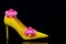 Stylish female yellow suede stiletto heel shoe decorated with pink orchids on dark background 