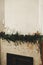 Stylish fireplace mantel decorated with christmas branches, bells garland, wooden ornaments and house decoration. Festive rustic