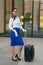 Stylish full length flight attendant in uniform with white gloves goes to work with a suitcase