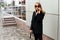 Stylish girl in black clothes, glasses, stands on the street and talks on the phone