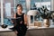 A stylish girl in a black dress sits on the windowsill by the window with a book in her hands