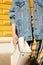 Stylish girl in a denim jacket in a hurry, waving a white square bag. Street lifestyle.