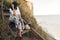 Stylish girl in fashionable look sitting on wooden stairs on beach cliff at sea in sunny light. Happy young boho woman in hat with