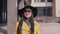 Stylish girl with a good mood in a yellow raincoat hat and glasses comes with luggage