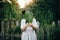 Stylish girl in linen dress holding big green leaf at face at wooden fence and grass. Portrait of boho woman in hat posing with