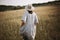 Stylish girl in linen dress walking among herbs and wildflowers in sunny meadow in mountains. Boho woman relaxing in countryside,