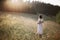 Stylish girl in linen dress walking among wildflowers in sunny meadow in mountains. Boho woman relaxing in countryside flowers at