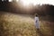 Stylish girl in linen dress walking among wildflowers in sunny meadow in mountains. Boho woman relaxing in countryside flowers at