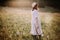 Stylish girl in linen dress walking among wildflowers in sunny meadow in mountains. Boho woman relaxing in countryside flowers at