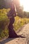 Stylish girl in long dress with rustic bouquet walking in meadow in sunset