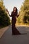 Stylish girl in long dress with rustic bouquet walking in meadow in sunset