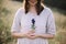 Stylish girl in rustic dress holding wildflower in hand, standing in sunny meadow in mountains. Boho woman gathering gentiana