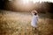 Stylish girl in rustic dress walking in wildflowers in sunny meadow in mountains. Boho woman relaxing in countryside flowers at