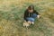 Stylish girl sitting on the field with a dog and stroking. Playing with a mongrel dog in the field, top view. Street animals