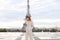 Stylish girl standing near Eiffel Tower in white overalls.