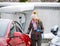 Stylish girl stands near her red electric car and waits for the car to charge. Connecting the plug of the electric