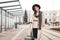 Stylish girl with a suitcase stands at a city stop awaiting a tram