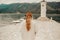 A stylish girl in a warm white suit walks on the island near the lighthouse. Travel, Montenegro