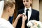 Stylish gorgeous bride putting on  boutonniere on elegant groom at church ceremony