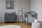 Stylish grey baby room interior with wooden furniture, white scandinavian ladder and teddy bear on pouf, real photo with copy