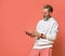 Stylish grey-haired hipster man in white hoodie standing and looking at smartphone display