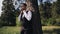 Stylish guy in a white shirt and vest stands in the woods by a tree and straightens his tie. Beautiful young man in nature