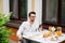 Stylish handsome man with glasses having breakfast in his country house on the veranda