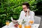 Stylish handsome man with glasses having breakfast in his country house on the veranda