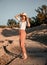 Stylish happy attractive smiling woman posing in desert sand dressed in white clothes wearing straw hat. Travel safari