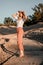 Stylish happy attractive smiling woman posing in desert sand dressed in white clothes wearing straw hat. Travel safari