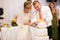 stylish happy bride and groom cutting and tasting fabulous wedding cake in a restaurant